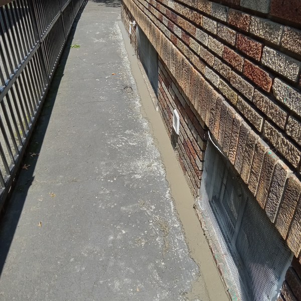 A sidewalk bordered by a brick wall and a fence.